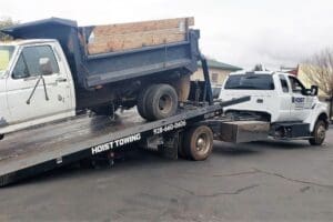 A secure Hoist Towing flatbed truck loading an abandoned dump truck onto the tow bed for disposal.