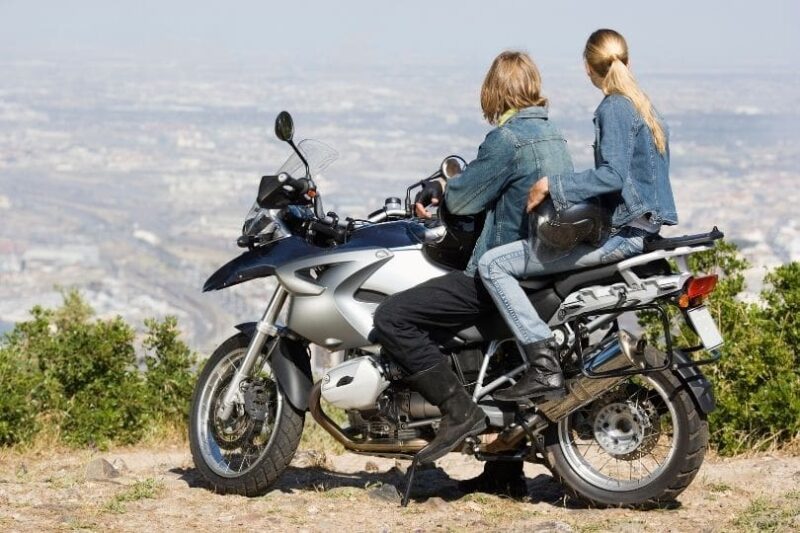 Two people on a motorcycle parked hilltop looking over the city
