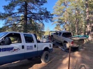 Hoist Towing 4x4 recovery truck alongside a flatbed tow truck with its tilted bed loading a vehicle on a Northern Arizona forest trail.