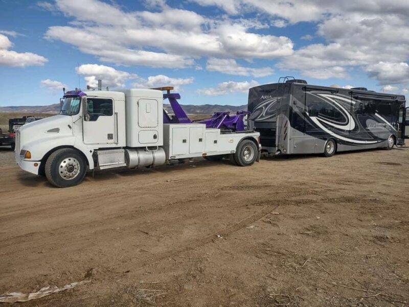 Hoist Towing heavy duty semi truck wrecker recovering a large luxury motorhome from a dirt lot in Arizona