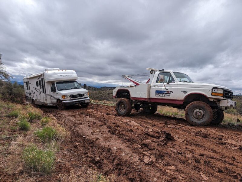 Hoist Towing heavy duty wrecker performing a slick mud extraction for a smaller RV sliding sideways while being winched onto a dirt road.