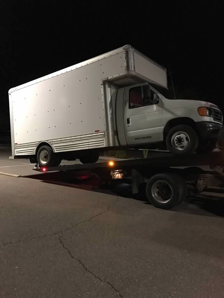 A commercial box truck is safely loaded on the tilted flatbed of our tow truck.