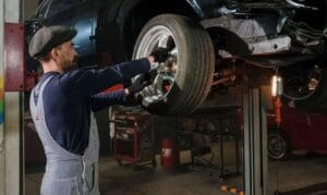An auto technician using a hydraulic lift to perform a routine tire safety inspection and wheel rotation service.
