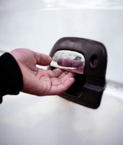 A close-up view of a person reaching out to check a door handle after realizing they are locked out of their vehicle.