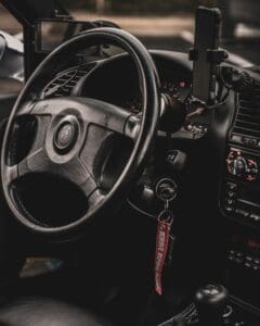 A close-up view of a car key left in the ignition switch with a red embroidered remove before flight keychain.