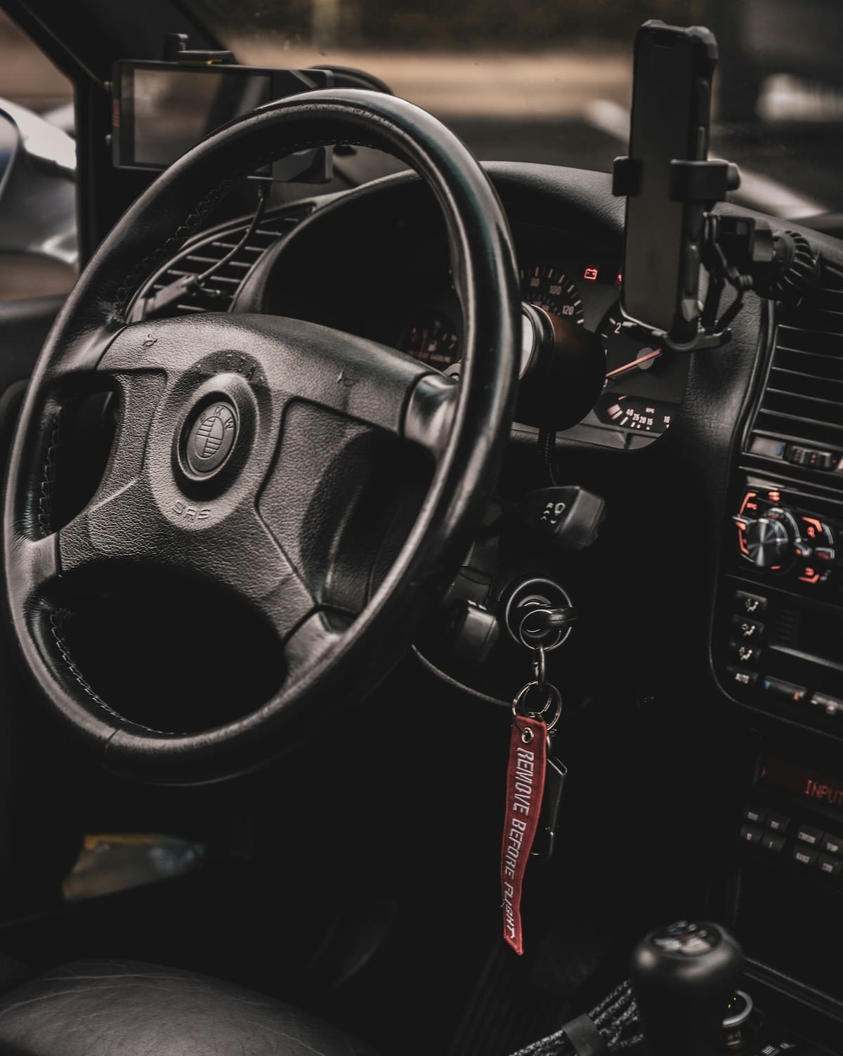 A close-up view of a car key left in the ignition switch with a red embroidered remove before flight keychain.